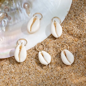 Detail of five cream shell hair rings with gold loops on a sandy beach background