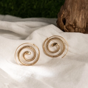 Detailed close-up of golden snake-shaped ear cuffs on natural wood and white linen