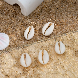 Set of five natural cowrie shell pendants with golden rings on beach sand and glass surface