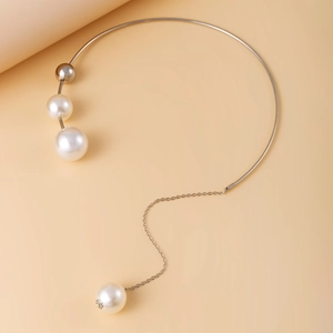 Detail van zilveren torque-halsketting met parelkralen en asymmetrische hangende ketting