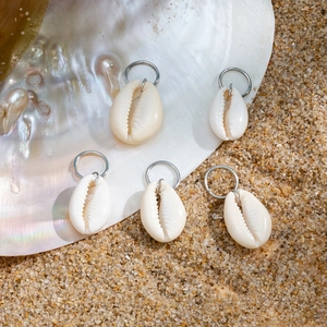 Set of five natural white cowrie shell hair clips with silver rings on beach background