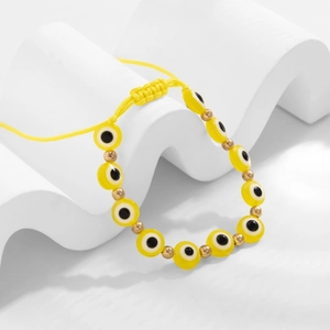 Détail du bracelet œil protecteur jaune avec perles dorées sur support blanc ondulé