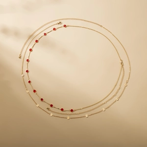 Double-layered gold body chain with red rhinestones and round sequins on beige background