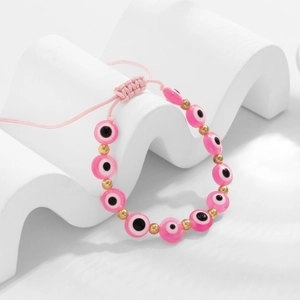 Détail d'un bracelet tressé rose avec perles mauvais œil et perles dorées ajustables