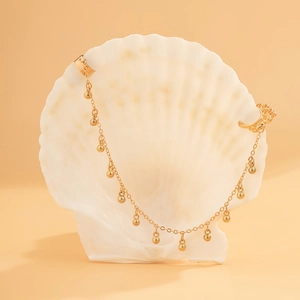 Detail einer goldenen Earcuff mit hängenden Perlenketten an einer Dekomuschel