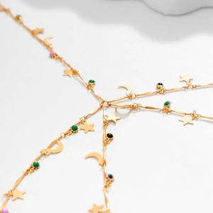 Detail of gold body chain featuring star and moon charms with colorful beaded accents