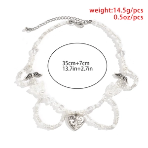 Detalle del collar de cuentas blancas con colgantes de corazón hueco y mariposa de plata