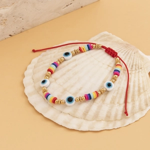 Bracelet perlé œil maléfique bohème avec cordon rouge sur fond de coquillage