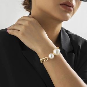 Detailaufnahme eines dicken Goldkettenarmbands mit zwei großen weißen Perlen am Handgelenk