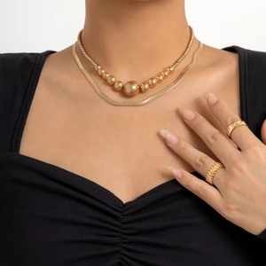 Detail van gelaagde gouden kralen- en slangenkettingen gedragen met geometrische ringen