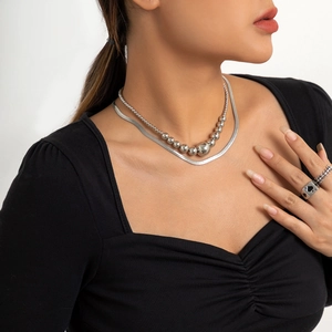 Detail van zilveren slangenketting en gelaagde kralenketting met metalen ringen