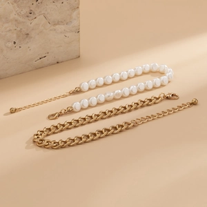 Détail d'un ensemble de bracelets de cheville en perles et chaîne dorée sur pierre