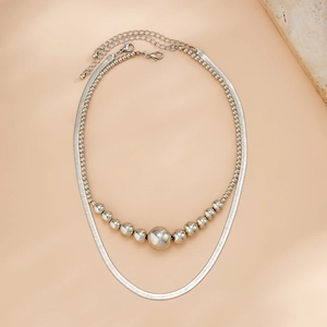 Dubbellaagse zilveren kralenketting met slangenketting op een beige achtergrond