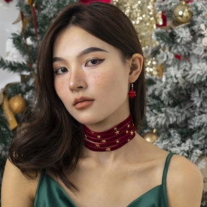 Detail van rode fluwelen choker met gouden sterren en bijpassende strikoorbellen voor Kerst