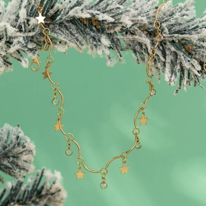 Detailopname van gouden sterhangers en kristallen aan ketting met feestelijke dennennaalden