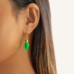 Gros plan de boucles d'oreilles ampoule verte avec crochets dorés portées par un mannequin