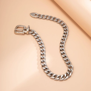 Close-up of silver-tone belt buckle clasp and thick curb chain necklace on a soft orange base