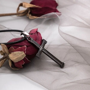 Gothische schwarze Kreuzkette mit Nieten auf einer getrockneten roten Rose und grauem Netz