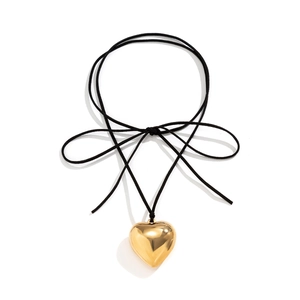 Detail of mirror-polished gold heart pendant on a delicate black velvet ribbon bow