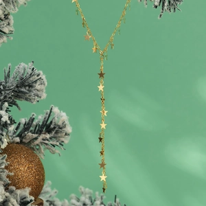 Detail van gouden Y-vormige ketting met sterhangers tegen een feestelijke groene achtergrond