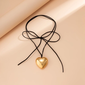 Macro shot of polished gold heart pendant with black cord bow on a warm beige background