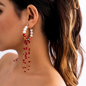 Close-up of bohemian hoop earrings with white pearls and long red beaded tassels on model