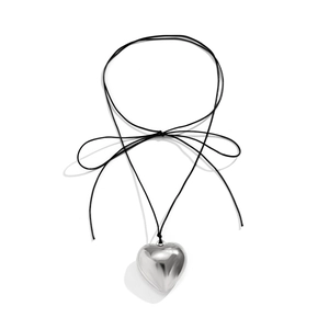 Detailed macro shot of a polished silver heart pendant with a black velvet ribbon bow