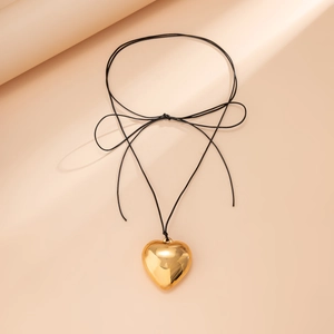 Detailed close-up of 3D gold heart pendant with black cord bow on a neutral background