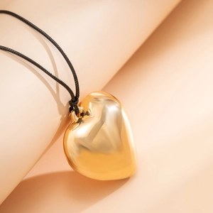 Macro shot of 3D polished gold heart pendant on adjustable black woven cord necklace