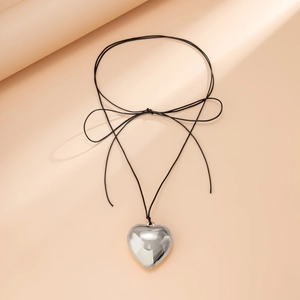 Close-up of a silver 3D heart pendant on a black cord necklace with a bow knot detail