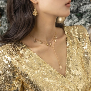 Detail van sterrenketting en kerstboomoorbellen op een model in een gouden feestelijke jurk