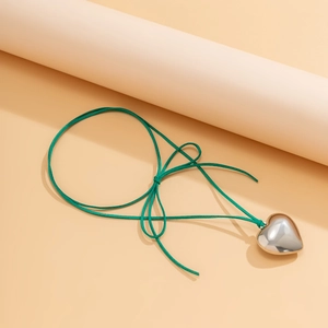 Detail of a large silver heart pendant with a green suede cord on a warm toned background