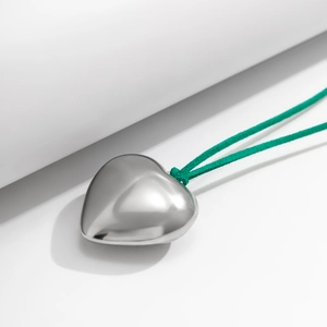 Detail of a large silver heart pendant with vibrant green adjustable cord necklace
