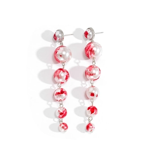 Detailed view of long white pearl drop earrings with artistic red blood splatter texture