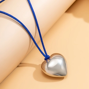 Macro shot of a polished silver heart pendant with dark blue suede cord on a display stand