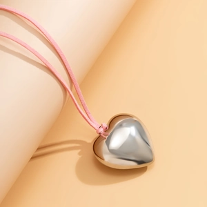 Close-up of a glossy silver heart pendant with a soft pink cord on a neutral background