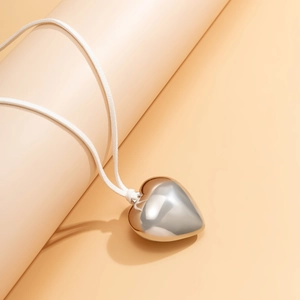 Macro shot of 3D puffy silver heart pendant with soft white suede cord necklace detail