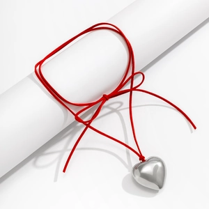 Close-up of a silver heart pendant on a red cord tied in a bow around a white cylinder