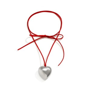 Detail view of large silver heart pendant on red cord necklace with elegant bow knot