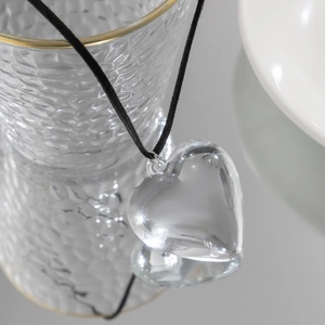 Detail of transparent 3D glass heart pendant on black cord hanging on a glass rim