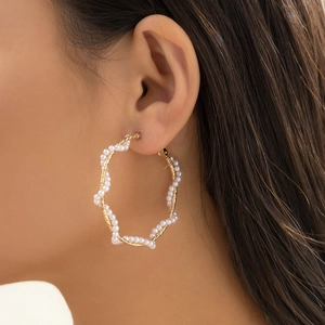 Close-up of a large gold twist hoop earring featuring embedded white pearls on model