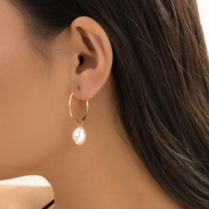 Close-up of golden hoop earring with a baroque pearl drop on model's ear