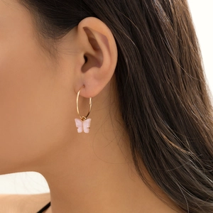 Close-up of a woman wearing gold hoop earrings with delicate pink butterfly charms