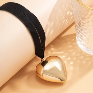 Detail of a large gold heart pendant with mirror finish on a black ribbed choker ribbon