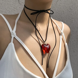Close-up of a red heart pendant choker with black cord on a model in natural sunlight