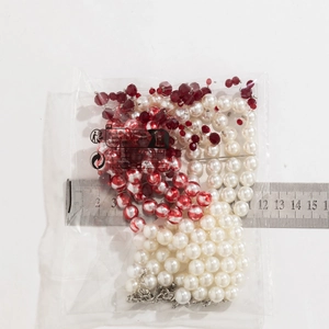 Detail of layered white pearl necklace with red crystal beads measured by a steel ruler