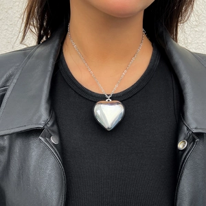 Close-up of a large polished silver heart pendant necklace on a black leather jacket