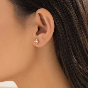 Detail of star-shaped gold stud earring with sparkling round zircon on model's ear