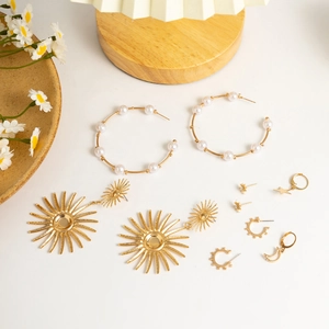Detail of gold earring set featuring stars, moons and pearls on a white surface
