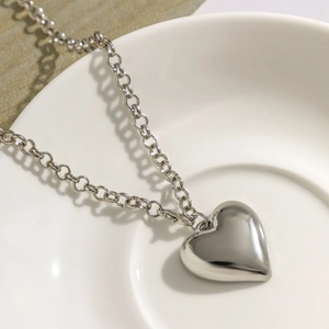 Close-up of polished silver heart pendant on a thick rolo chain necklace detail
